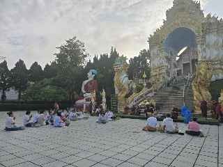 พุทธศาสนิกชนนั่งเรียงรายบนลานธรรมหน้าซุ้มประตูวิจิตรเพื่อเตรียมตักบาตร